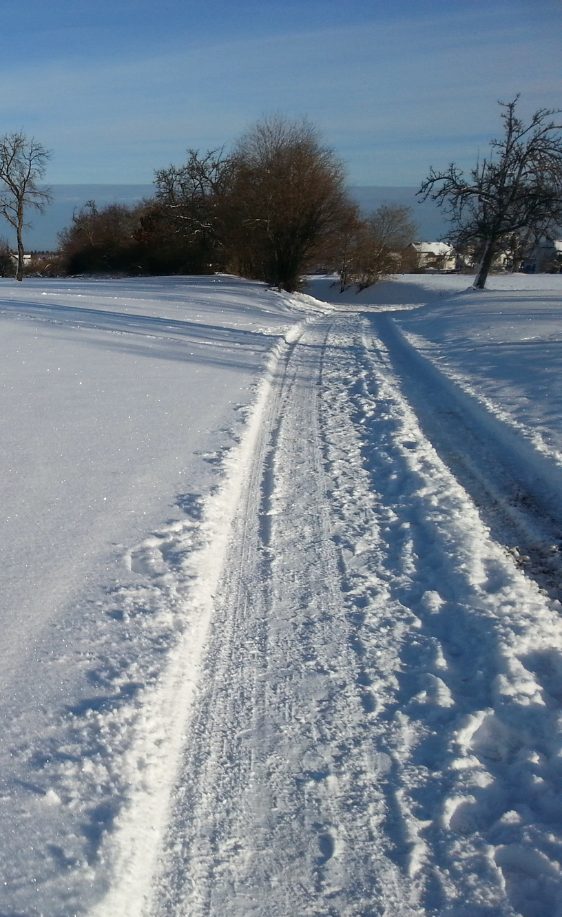 Eine schmale Straße mit einigen Zentimetern hohem, festgefahrenem, teilweise noch lockeren Schnee.