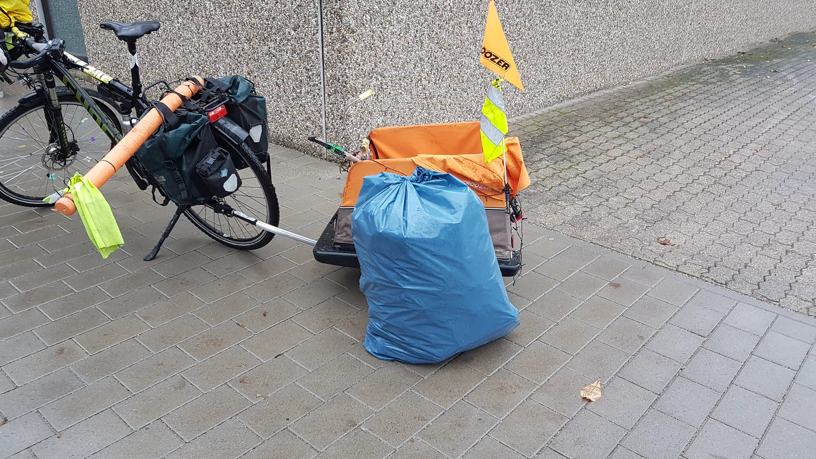 Gespann aus Fahrrad und Fahrradanhänger und davor steht ein voller Müllsack.
