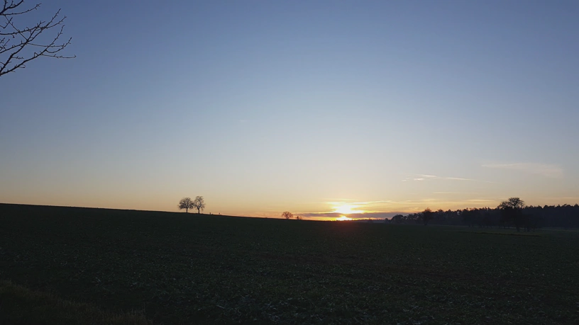 Landschaft (flaches Feld) mit Sonnenuntergang am Horizont.