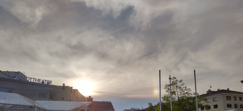 Sonne steht über der Stadt. Rechts ist irgendwo ein Teil eines Halo-Effekts zu sehen.
