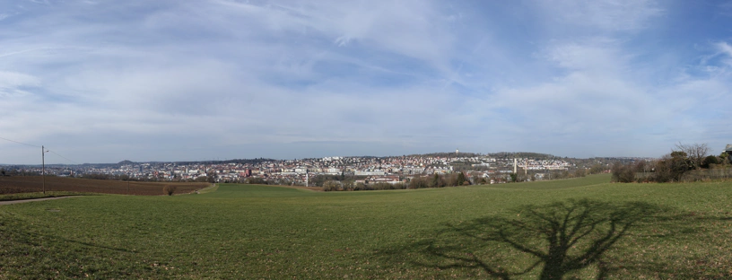 Landschaftspanorama mit blauem, bewÃ¶lkten Himmel und grÃ¼nen und braunen Feldern. Im Hintergrund die Stadt Pforzheim.