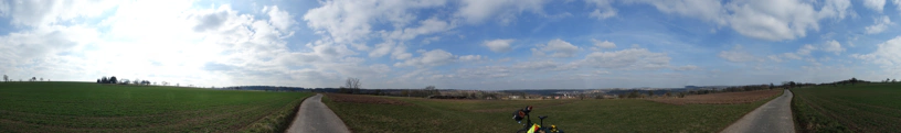 Panorama von einer Landschaft. In der Mitte steht ein Fahrrad. Wolken am Himmel. GrÃ¼ne Felder.